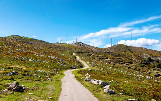 Winding path through Algarve hills with radio towers under a clear blue sky.