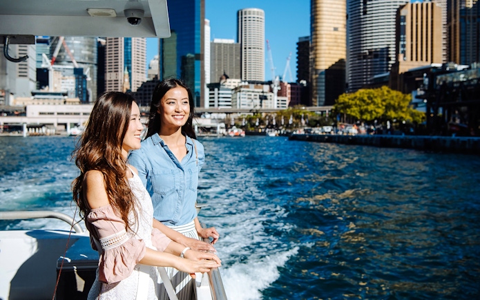 Two people enjoying a Sydney Harbour cruise with city skyline in the background.
