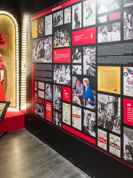 Exhibit at The Museum of Broadway featuring a red costume and historical Broadway posters.