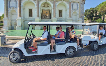 Golf cart with people touring near a historic fountain.