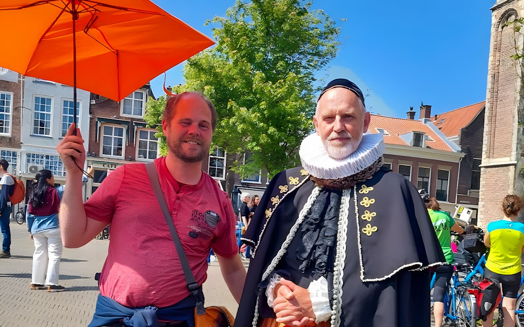 Tour guide with orange umbrella and man in historical costume in Delft.