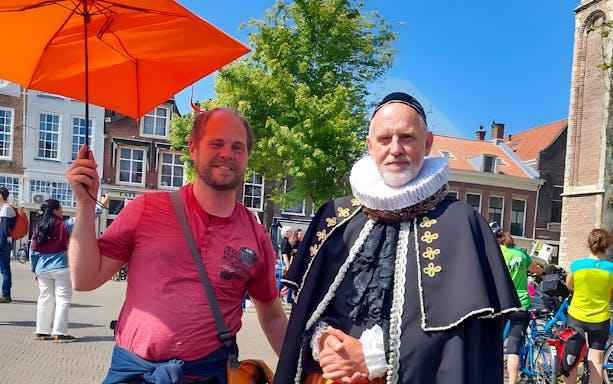 Tour guide with orange umbrella and man in historical costume in Delft.
