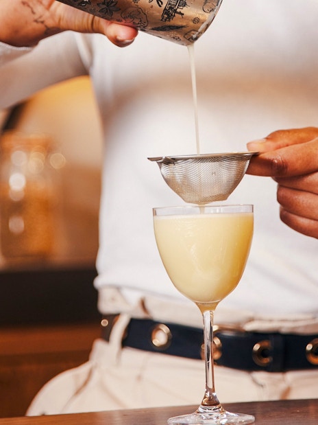 Pouring cocktail through strainer at Roe & Co Distillery.