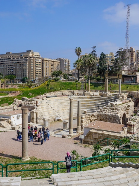 Ancient Roman Theatre ruins in Kom El-Deka, Alexandria, with cityscape in the background.