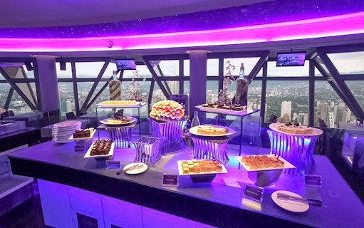 Buffet spread at Atmosphere 360 Revolving Restaurant with city view in background.