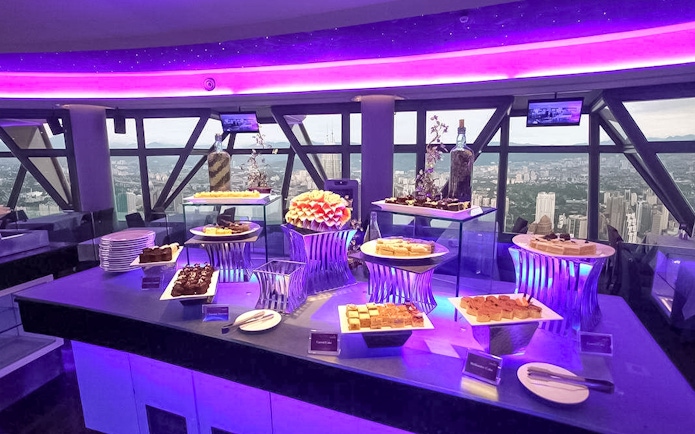 Buffet spread at Atmosphere 360 Revolving Restaurant with city view in background.
