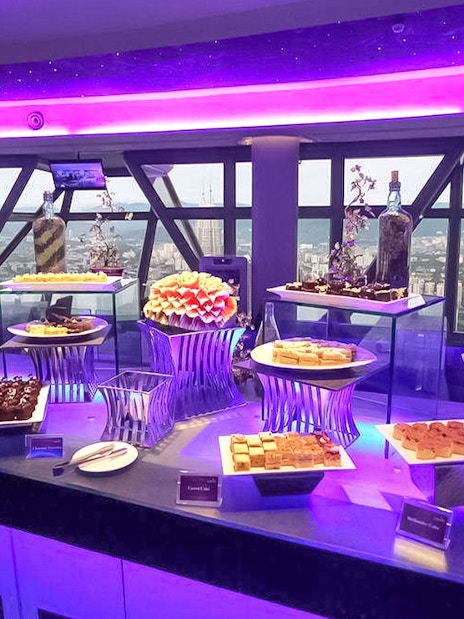 Buffet spread at Atmosphere 360 Revolving Restaurant with city view in background.