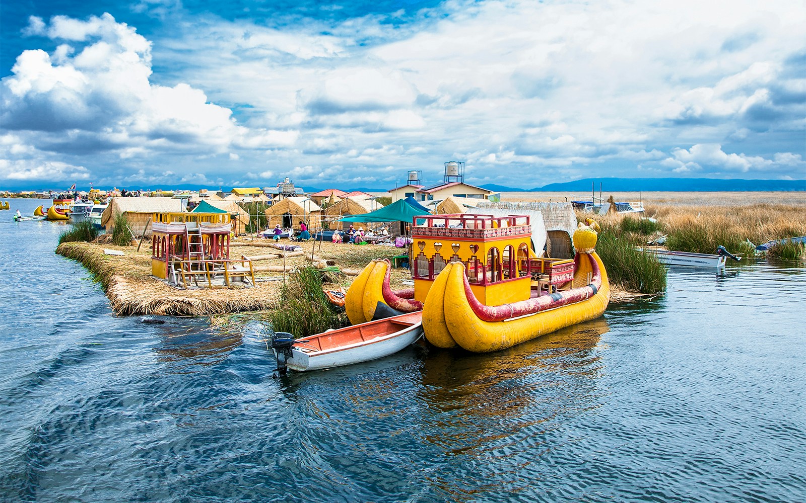 Group of tourists enjoying a Hop-on Hop-off tour at the serene Lake Titicaca in Peru, with traditional boats and distant mountains in view