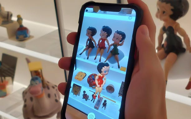 Hand holding phone displaying toy figures at MINT Museum of Toys.