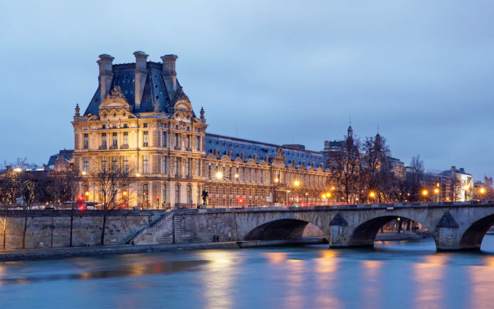 Louvre Museum and Seine River illuminated at night, Paris sightseeing cruise.