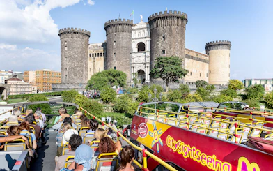 City sightseeing bus near Castel Nuovo, Naples, with tourists on board.