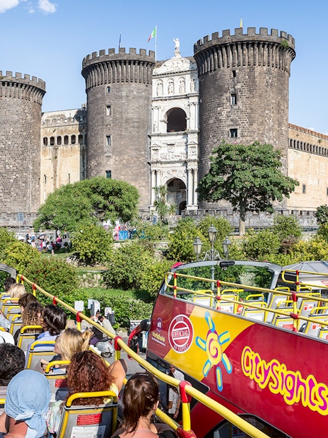 City sightseeing bus near Castel Nuovo, Naples, with tourists on board.