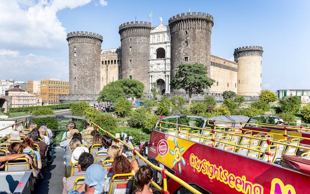 City sightseeing bus near Castel Nuovo, Naples, with tourists on board.