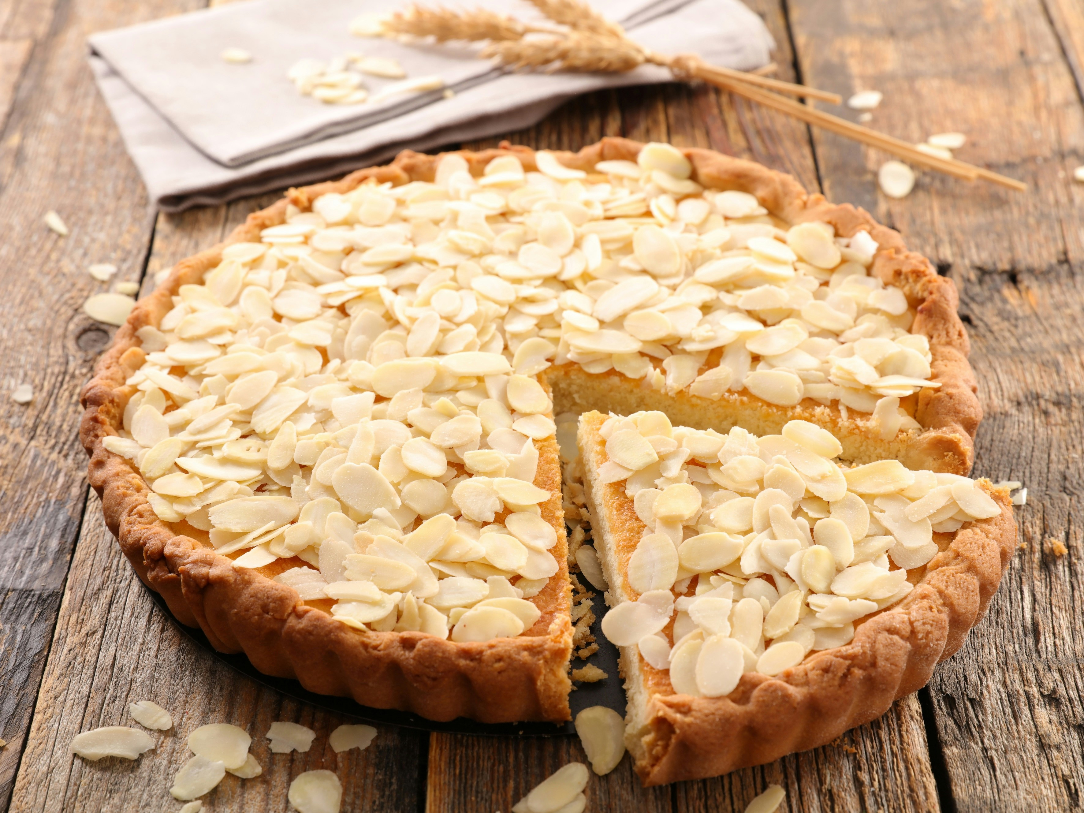 Almond cake on wooden table with sliced almonds on top.
