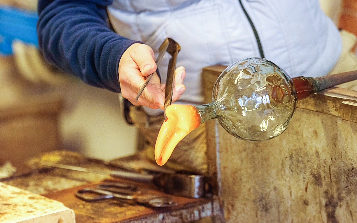 Glassblower shaping molten glass with tools in a workshop.