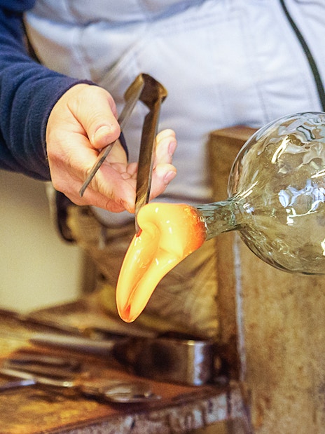 Glassblower shaping molten glass with tools in a workshop.