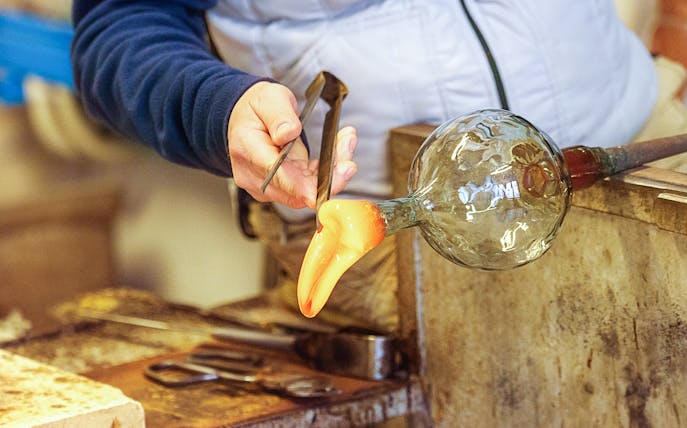 Glassblower shaping molten glass with tools in a workshop.