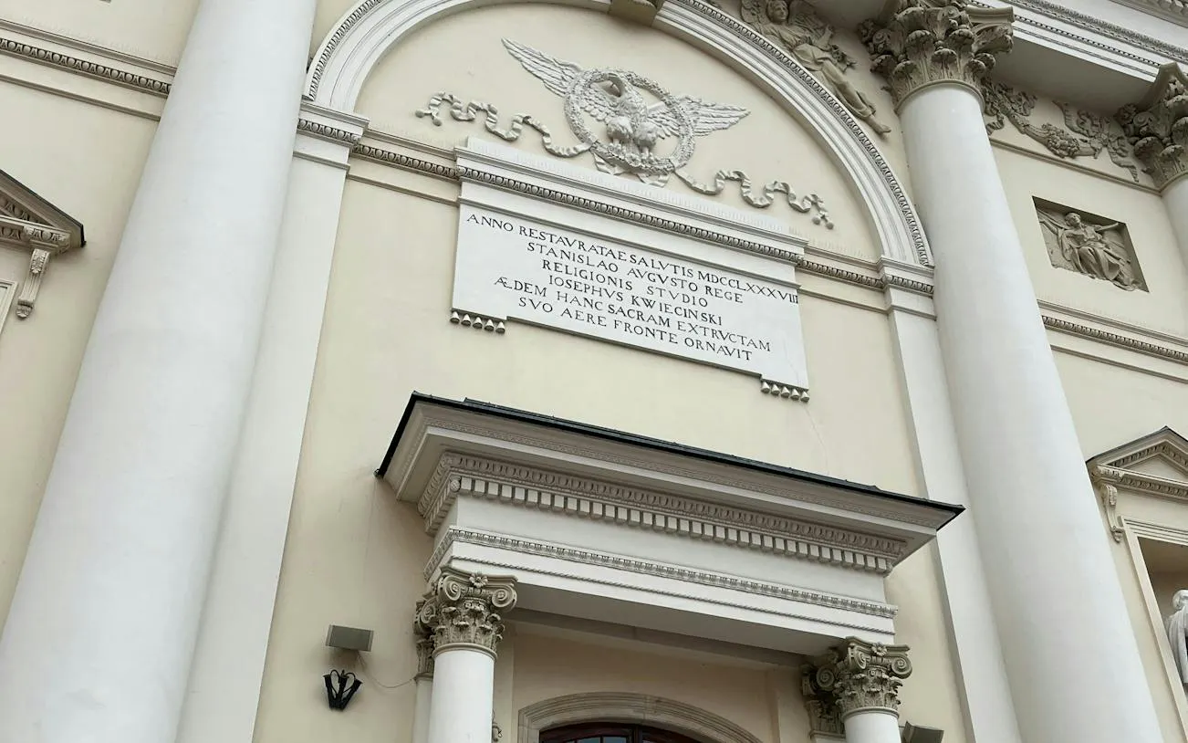 Facade of a historic building with Latin inscription, part of Warsaw Murder Mystery game.