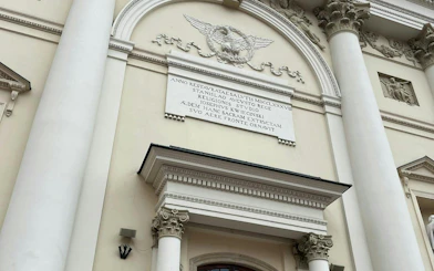 Facade of a historic building with Latin inscription, part of Warsaw Murder Mystery game.