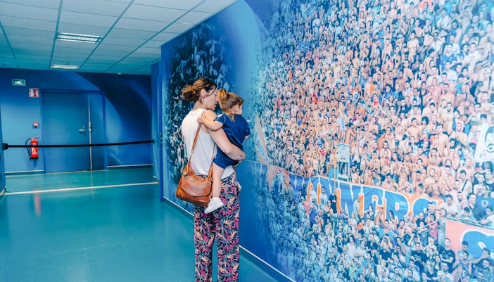 Mother and child viewing a mural of cheering fans at Velodrome Stadium tour.