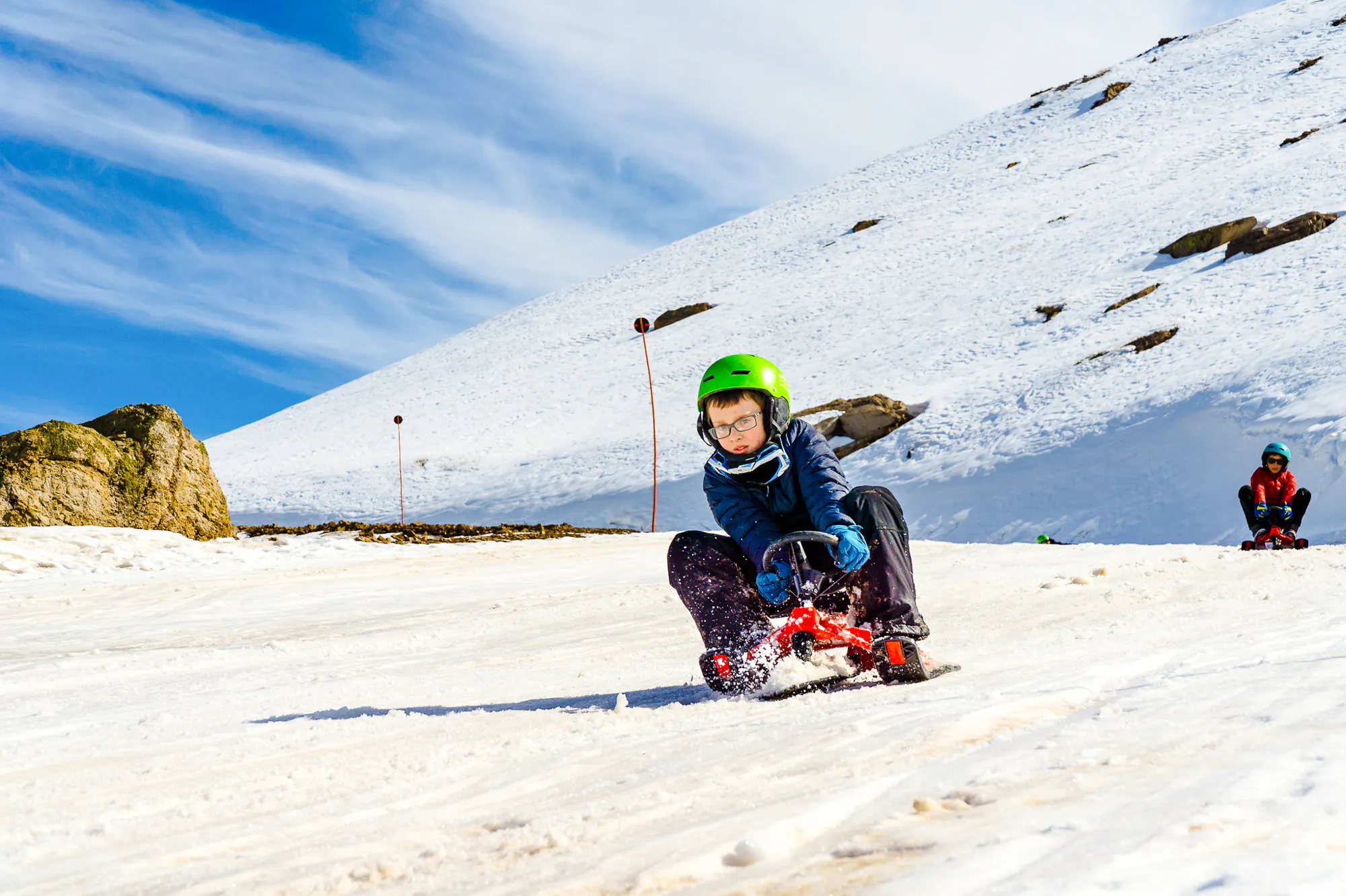 Child sledding on snow at Farellones Park, Santiago, with mountains in the background.