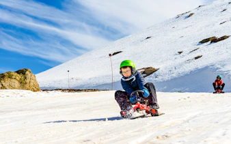 Child sledding on snow at Farellones Park, Santiago, with mountains in the background.