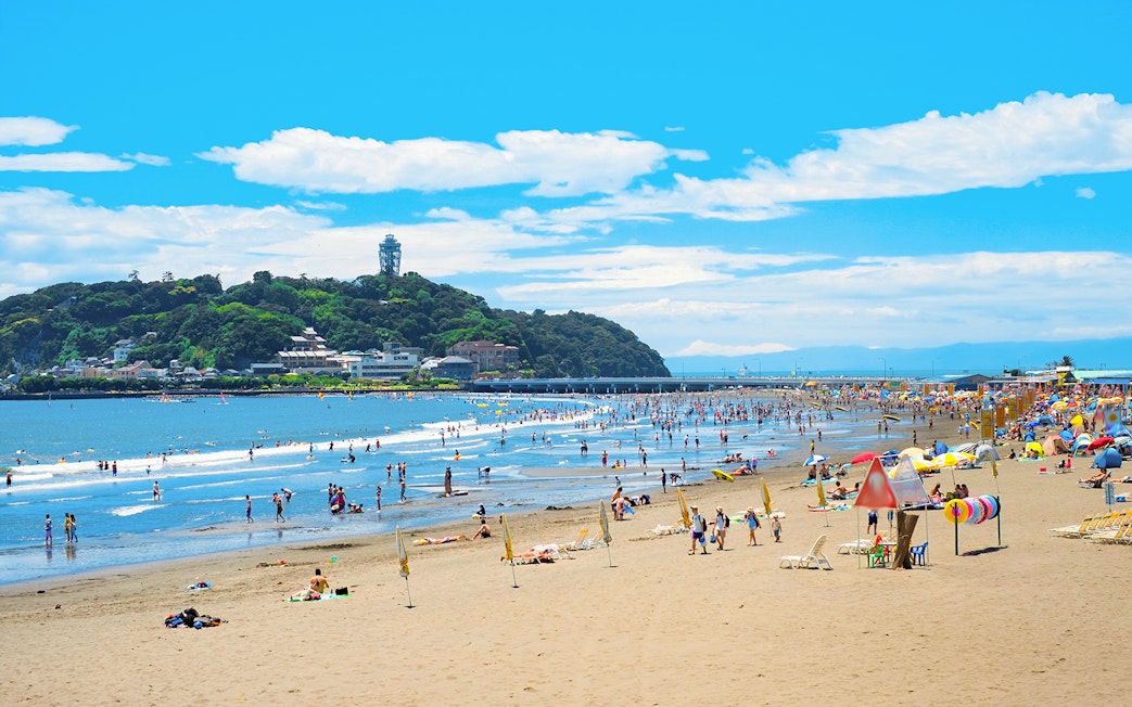 People enjoying Shonan Beach with Enoshima Island in the background.