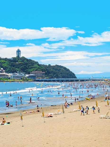 People enjoying Shonan Beach with Enoshima Island in the background.