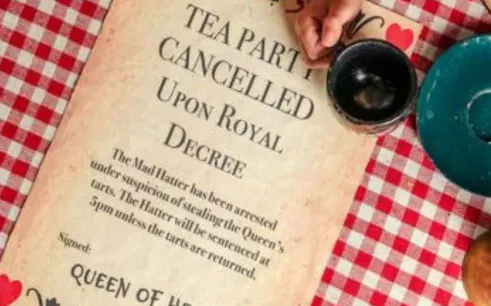 Tea party cancellation notice on checkered tablecloth at Alice in Puzzleland Dubai escape room.