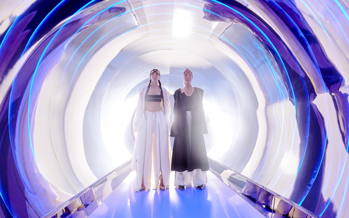 Women in high fashion at AYA Universe, Dubai, standing in a futuristic tunnel.