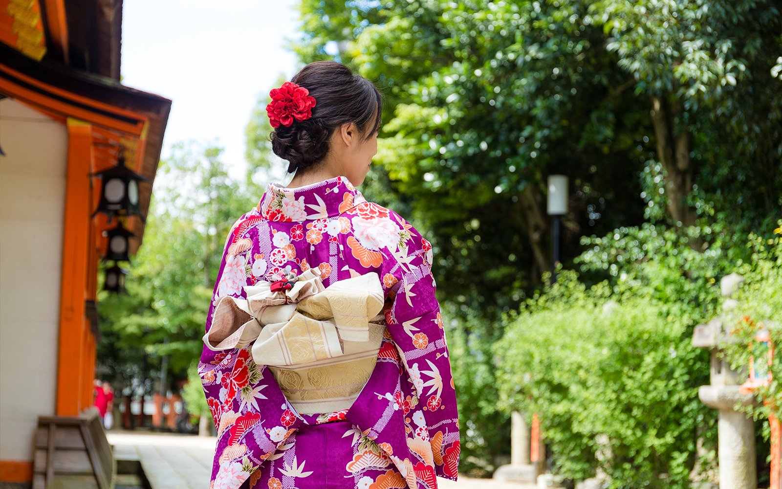 Young woman in a floral kimono walking through a Japanese garden.