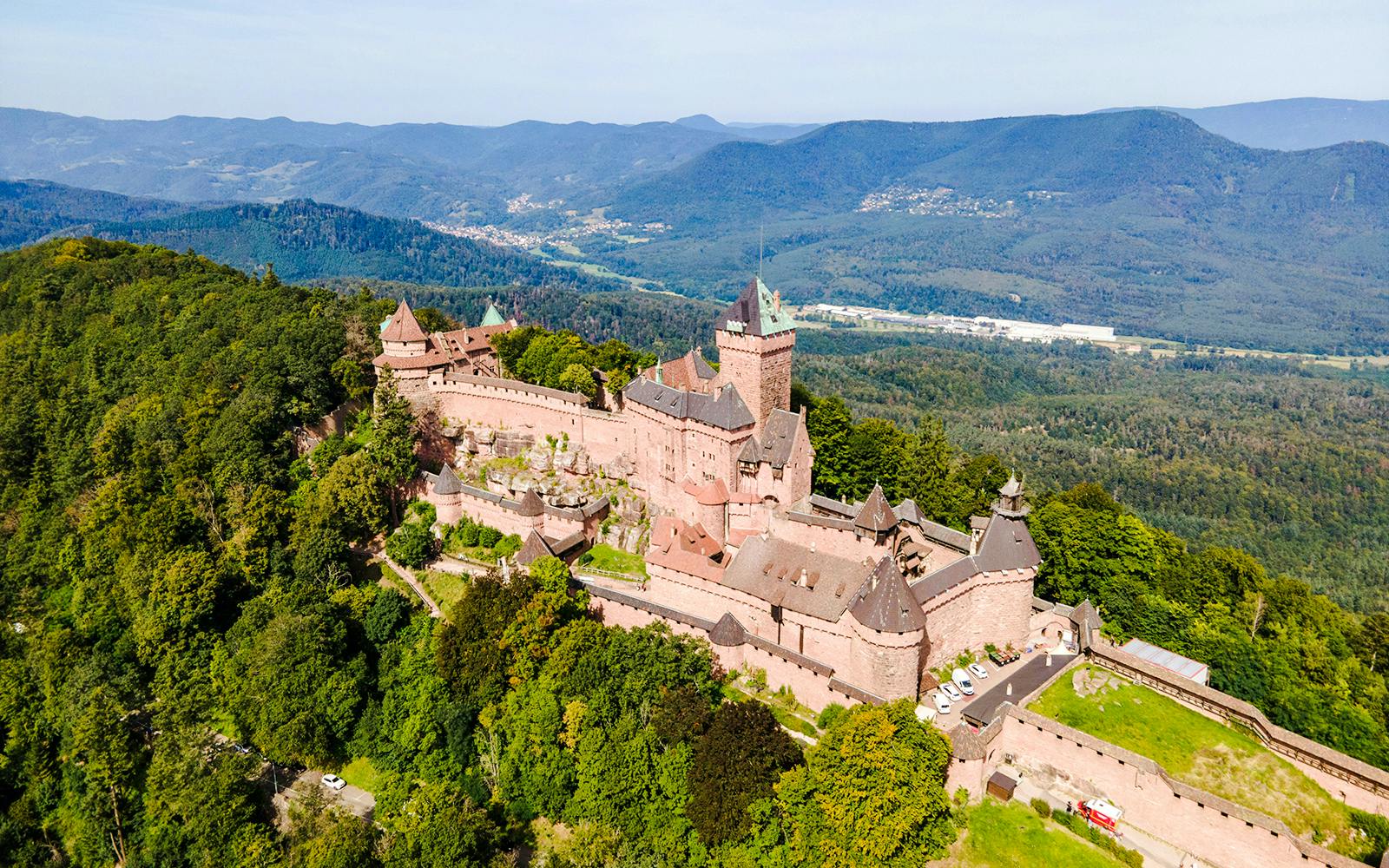 Haut-Koenigsbourg Castle in Alsace, France, surrounded by lush forest and distant mountains.