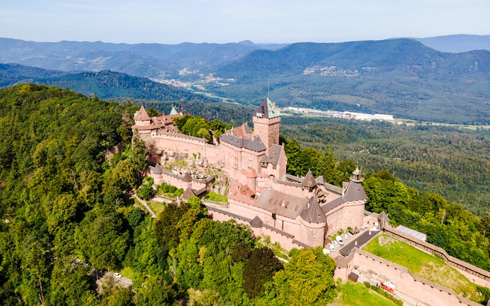 Haut-Koenigsbourg Castle in Alsace, France, surrounded by lush forest and distant mountains.