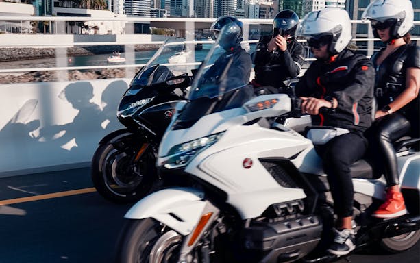 Motorcyclists riding on a bridge in Dubai with city skyline in the background.