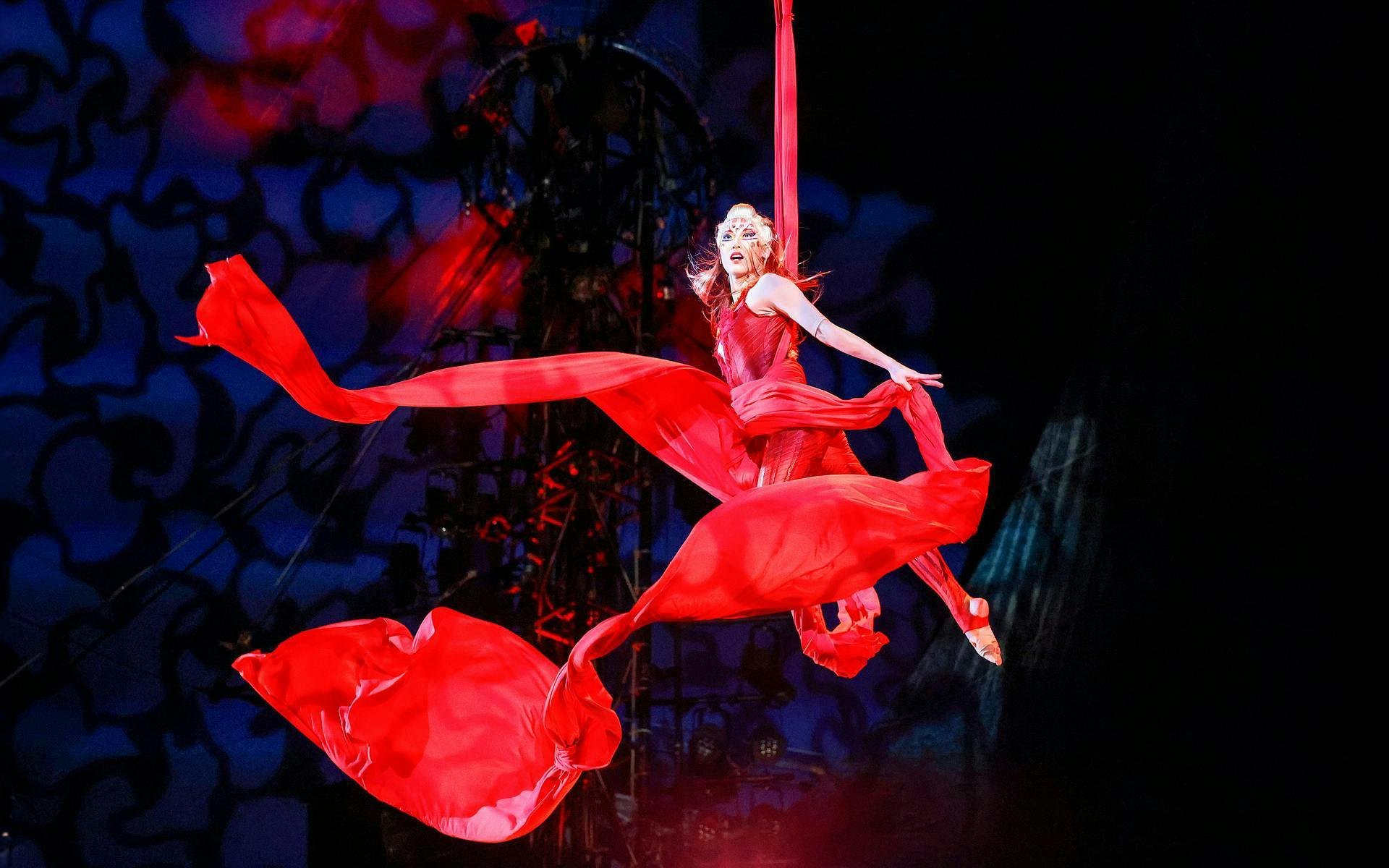 Performer in red costume suspended in aerial silk during Kooza stage show.
