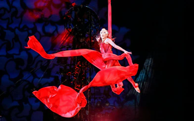Performer in red costume suspended in aerial silk during Kooza stage show.