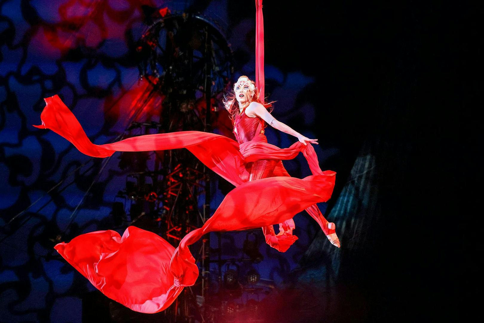 Performer in red costume suspended in aerial silk during Kooza stage show.