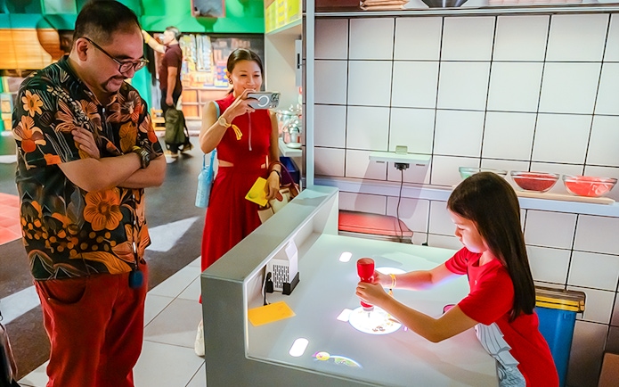 Family explores digital kitchen exhibit with interactive food projections.