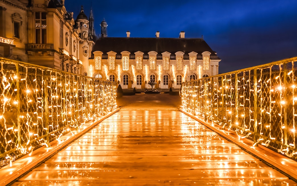 Chateau of Chantilly illuminated at night with festive lights on a bridge.