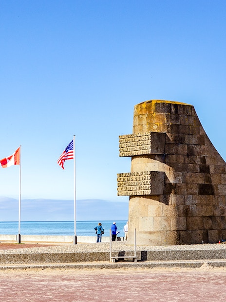 Monument and flags at Omaha Beach, Normandy, France, with ocean view.