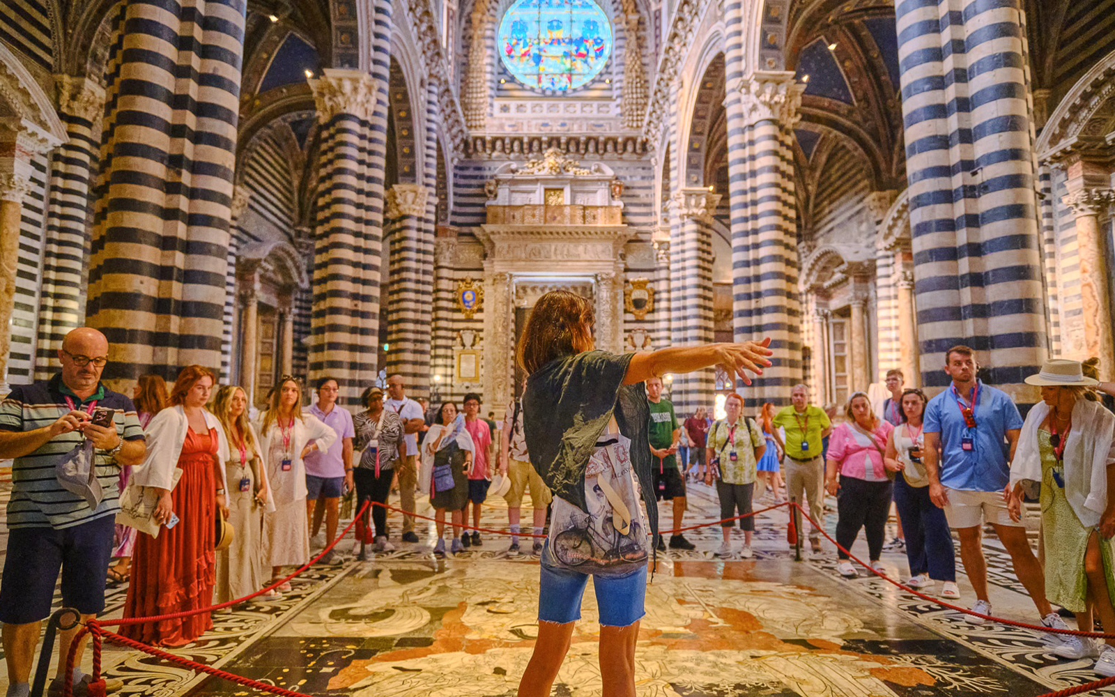Tour group inside Siena Cathedral with striped columns and stained glass window.