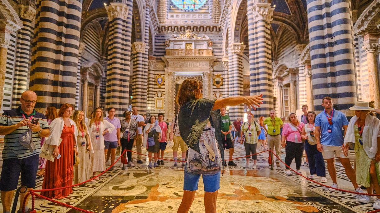 Tour group inside Siena Cathedral with striped columns and stained glass window.