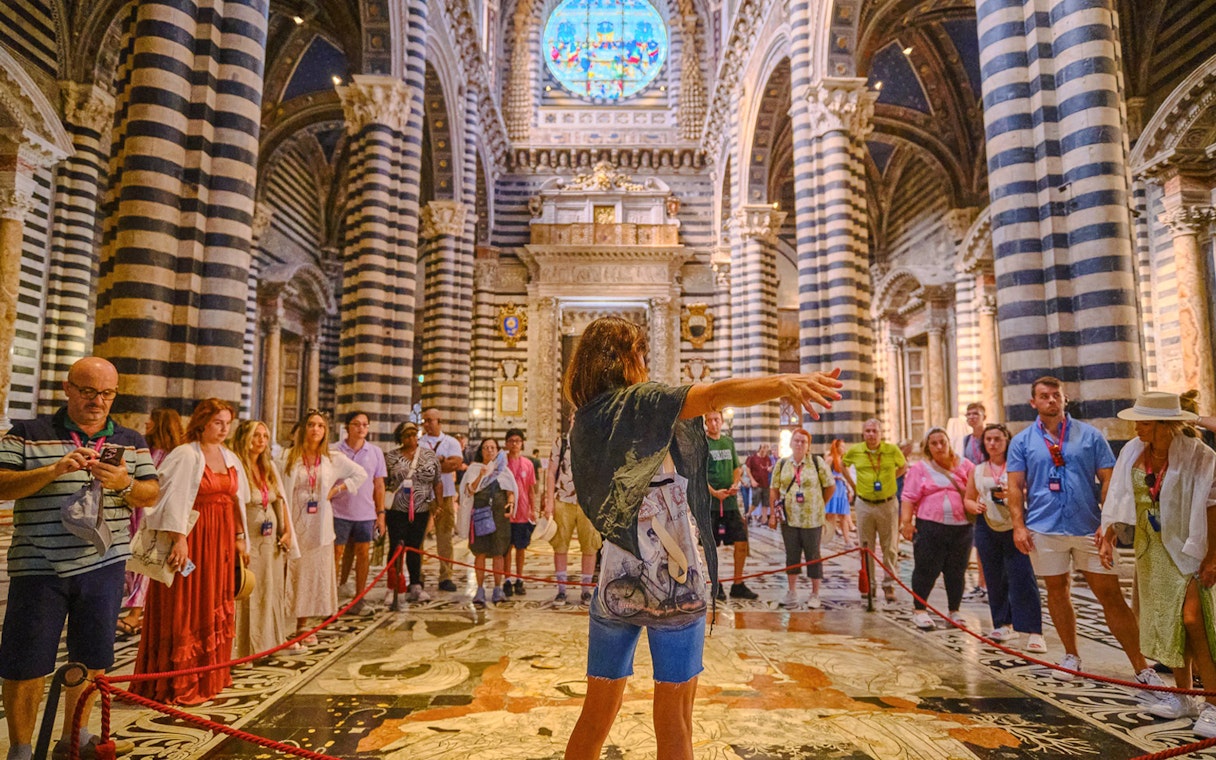 Tour group inside Siena Cathedral with striped columns and stained glass window.