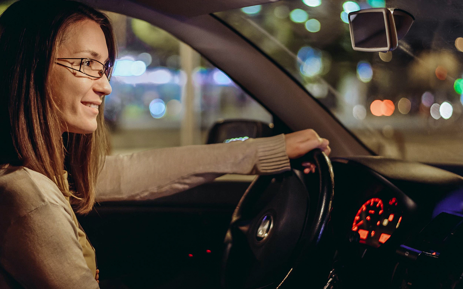Woman driving a car at night in a city with blurred lights in the background.