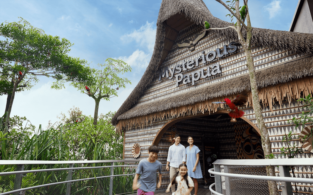 Entrance to Mysterious Papua aviary with visitors and colorful birds in trees.