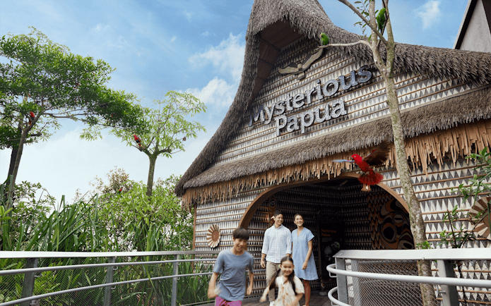 Entrance to Mysterious Papua aviary with visitors and colorful birds in trees.