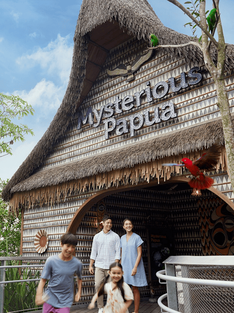 Entrance to Mysterious Papua aviary with visitors and colorful birds in trees.