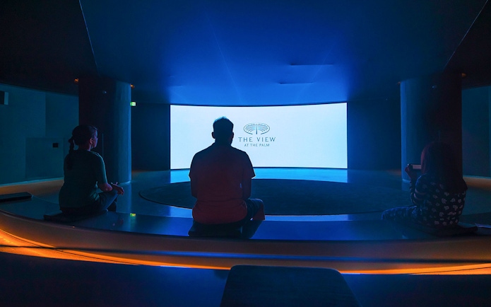 Visitors seated in a dark room facing a screen displaying "The View At The Palm" logo.