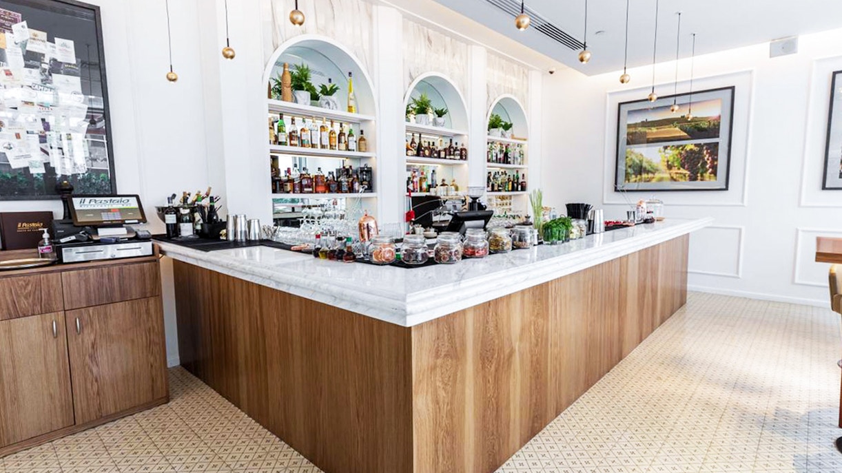 Bar area at Il Pastaio Restaurant, featuring a marble countertop and shelves with bottles, part of La Perle dinner package.