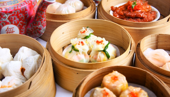 Variety of dim sum in bamboo steamers with a decorative teapot.